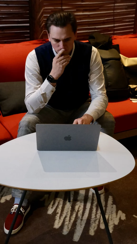 Paul, fondateur d'Atout Paul, souriant devant son ordinateur portable dans un espace de travail moderne.